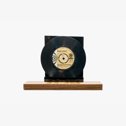 Black vinyl record mounted on a dark display stand atop a wooden base, shown head-on with the label visible.