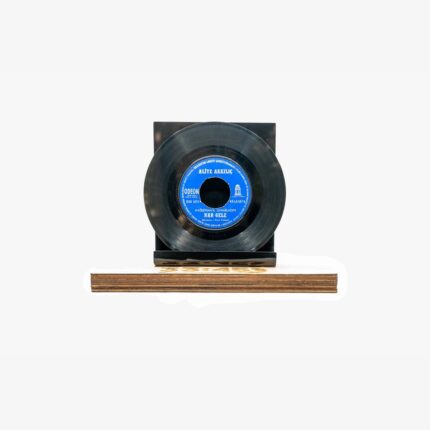 A black vinyl record mounted on a small black stand sitting on a wooden base, with a blue label in the center.