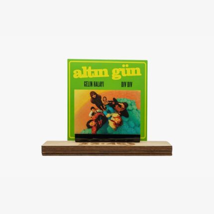 Bright green album cover with bold yellow title and the names Gelin Halayı and Div Div, displayed on a wooden stand. The cover features a colorful photo of a group of people.