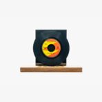2301450012B | 3345 Records Black vinyl record on a wooden display base with an orange-yellow label on the center.