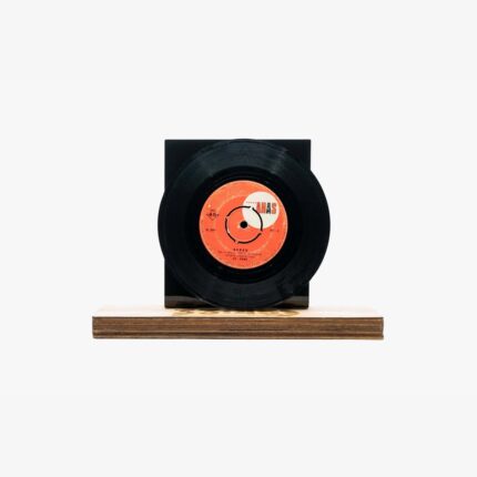 Black vinyl record mounted on a light wooden stand against a white background, its orange label visible at the center.
