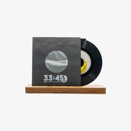 Black vinyl record partially slid out of a dark gray sleeve with a circular window, resting on a wooden base; the sleeve reads '33:45'.