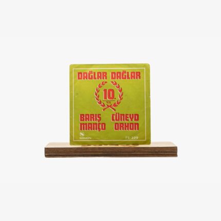Vintage green square album cover with red Turkish text 'Dağlar Dağlar' and '10. Yıl', featuring Barış Manço and Cüneyd Orhon, mounted on a wooden base.