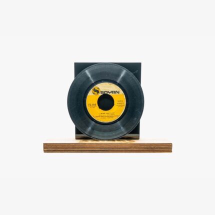 Black vinyl record mounted on a wooden base with a dark backdrop and a yellow label at the center.