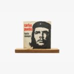 2301450038A | 3345 Records Album cover with a high-contrast Che Guevara portrait and the text 'carlos pueblo' and 'hasta siempre' on a beige background, resting on a wooden shelf.