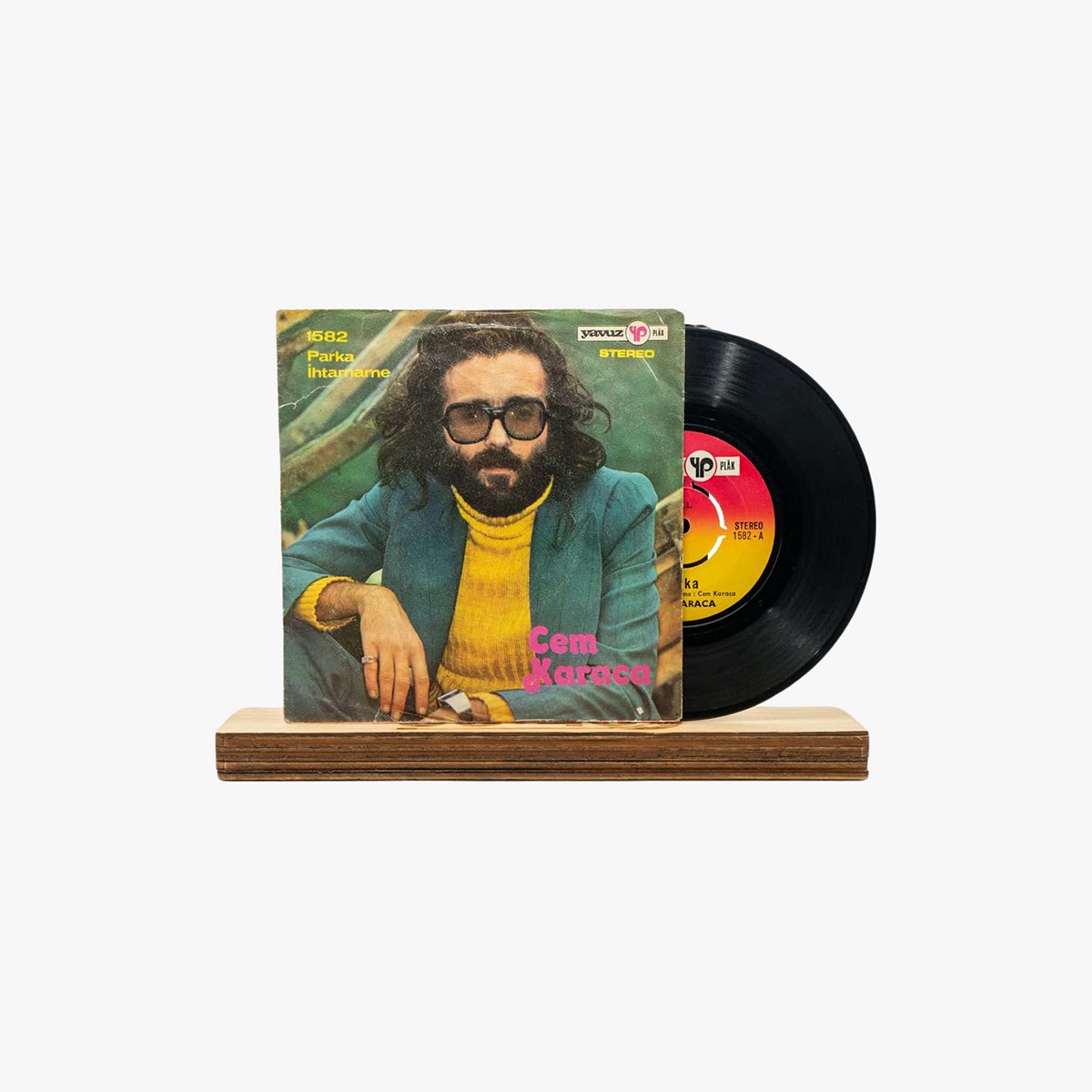 2301450049A | 3345 Records Vintage vinyl record with Cem Karaca album cover featuring a bearded man with glasses in a yellow sweater and blue jacket, on a wooden stand.