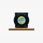 Vinyl record mounted on a black backing board resting on a wooden base for display.