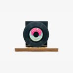 Vintage black vinyl record mounted on a wooden display base against a light background. The label hints at a Turkish release (Cem Karaca Kardaslar).