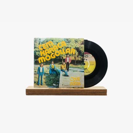 Vinyl LP with a colorful 'Cem Karaca Mogollar' cover displayed on a wooden stand with the record partially pulled out. Silkscreened text 'Obur Dünya' is visible on the cover edge.