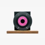 2301450079B | 3345 Records Black vinyl record with a pink center label mounted on a wooden display base.